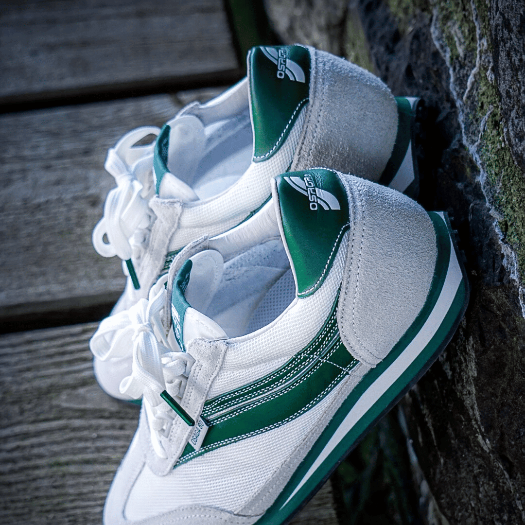 White and green sneakers leaning against a rock wall.