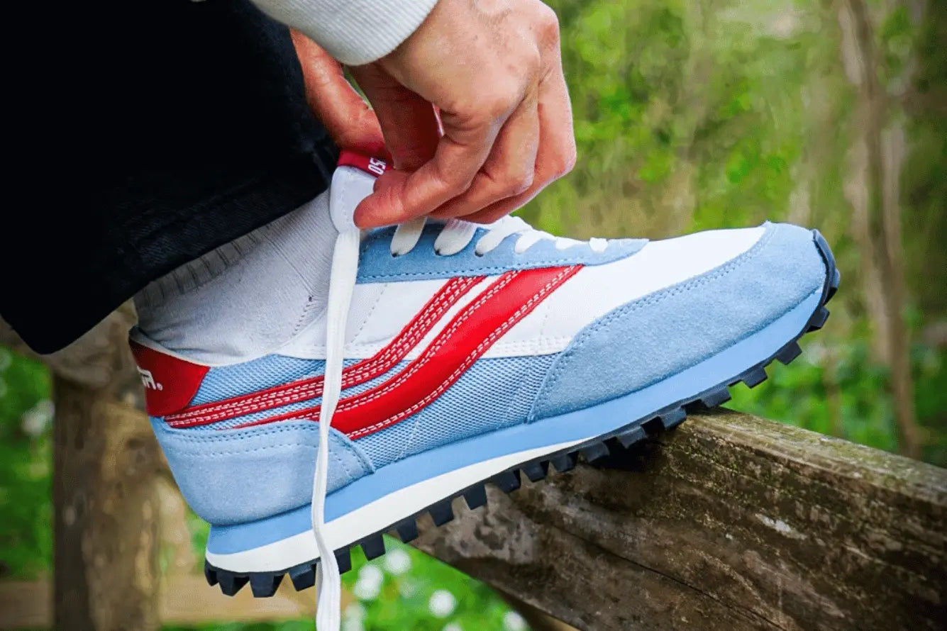 Person tying a light blue, white and red sneaker with a blurred natural outdoor background