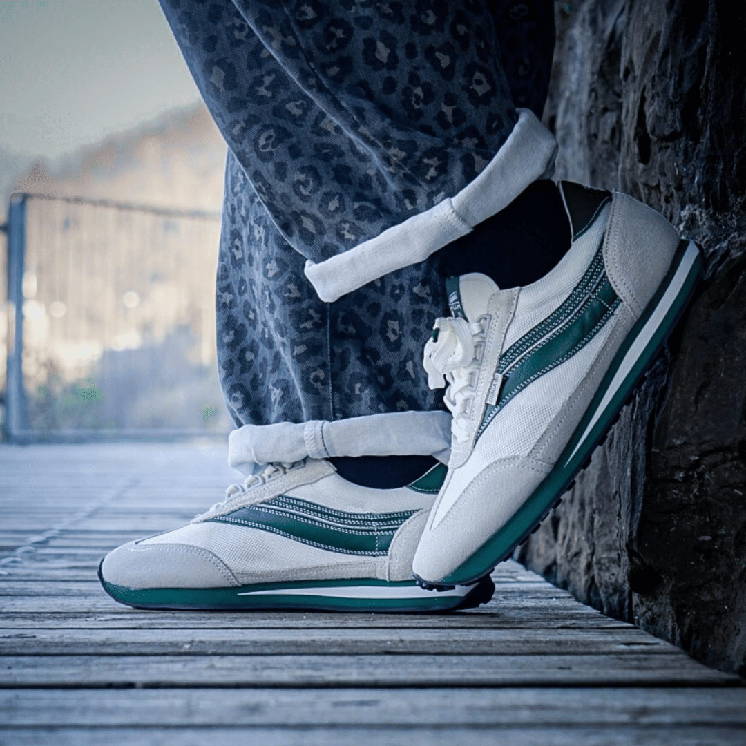 White and green retro sneakers worn by a person sitting by a mountain view