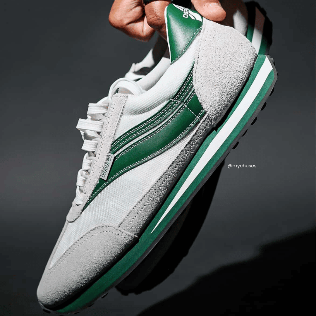 Gray and green sneakers held by a hand against a dark background