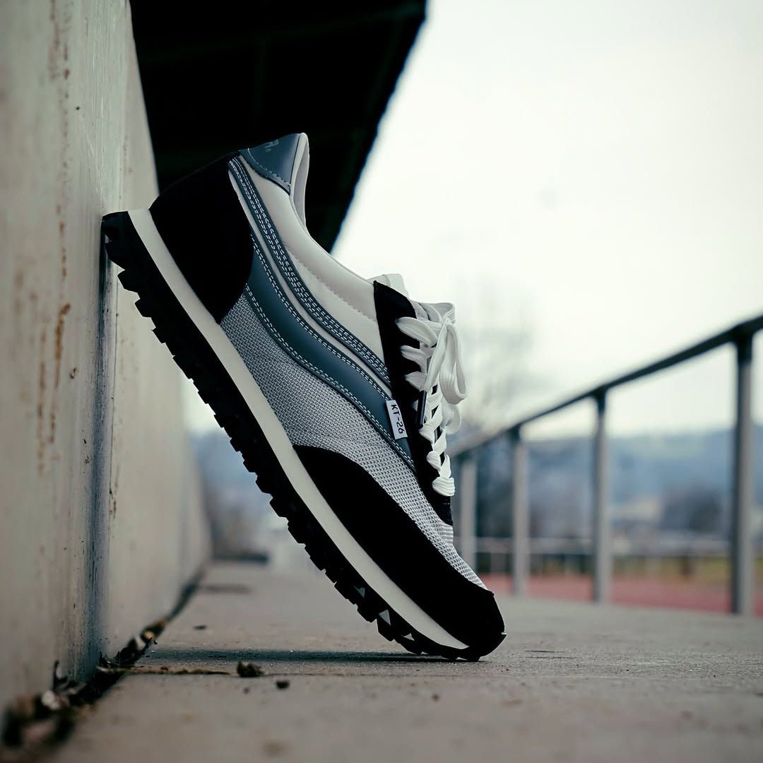 Black and white sneaker with blue accents on a concrete surface.
