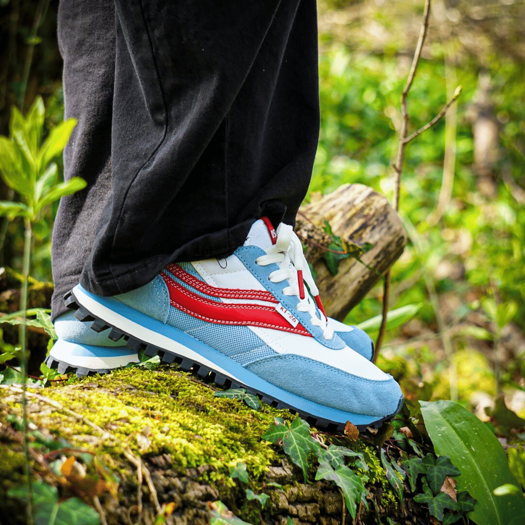 Blue and red running shoes on a person standing on a log in a forest setting