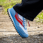 Blue, white, and red shoes with black rubber soles on a person's foot outdoors.