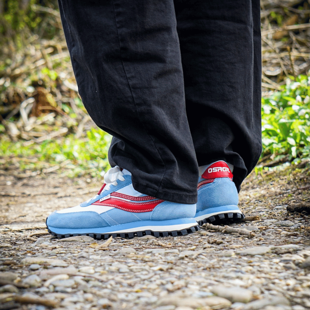 Person wearing white, blue, and red sneakers with 'Osaga' branding on a natural ground.