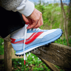 Person tying shoe laces with red metal anklets on a blue, white, and red sneaker outdoors.