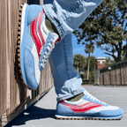 Person wearing blue and red sneakers with gum soles, standing on a wooden deck.